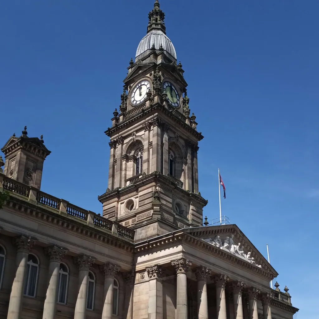 The clock tower and columned front of Bolton Town Hall on Victoria Square, under a clear blue sky